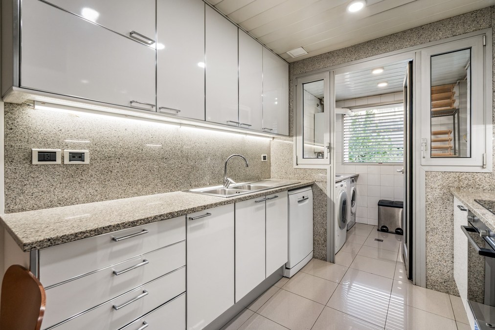 Cocina con muebles blancos, encimera de granito y salida al lavadero