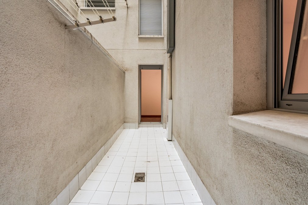 Patio interior del piso con suelo de baldosa blanca y tendedero